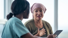A patient in a headwrap consulting with a doctor who is holding a digital tablet