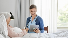 caregiver at patient bedside reviews prescription information with a virtual care prescriber on a tablet   