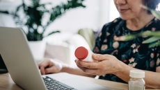 Patient checks pill bottle against her patient record on a laptop
