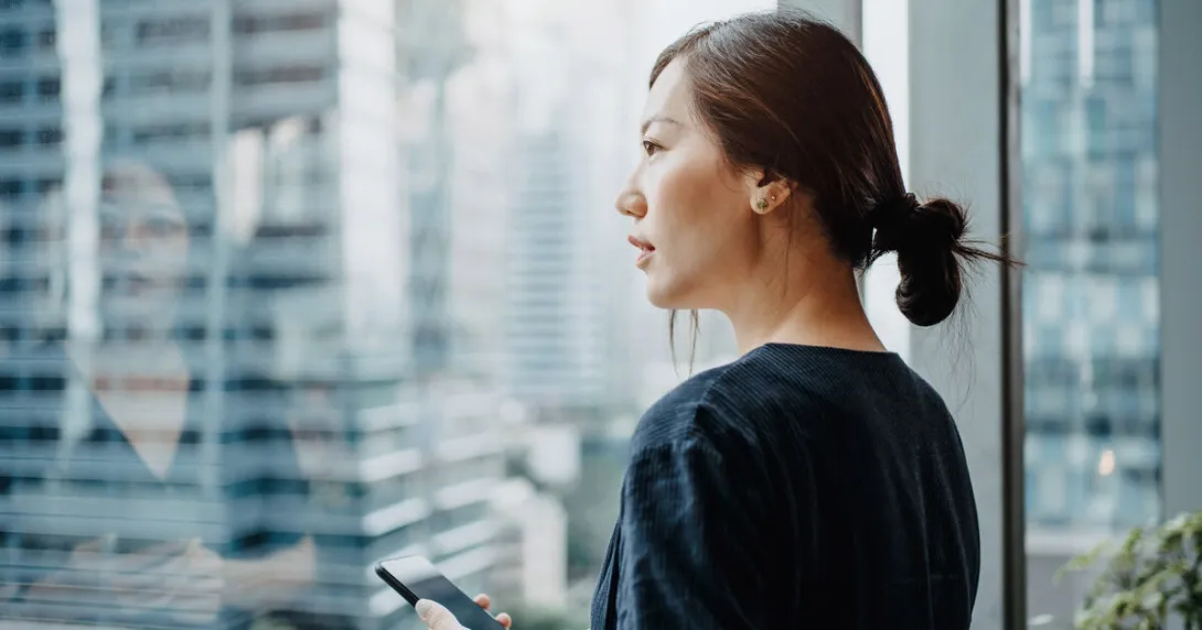 A person holding a smartphone staring outside the office window
